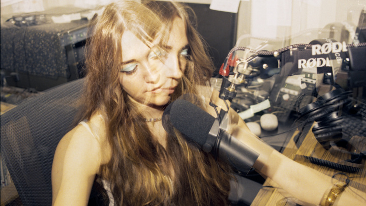 A multiple-exposure picture of a girl with blue eyeshadow and long, fringed hair, sitting in front of a radio microphone.
