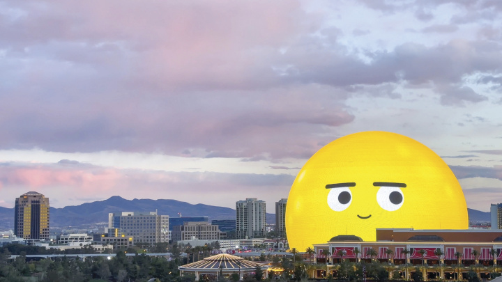 The Las Vegas Sphere, lit up as a yellow smiling emoji, against a dusky skyline.