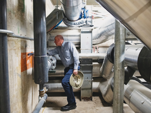 A man holds a hat while he makes an adjustment inside a power plant.