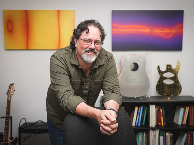 Russell Stoneback stands in front of his artwork and guitars.
