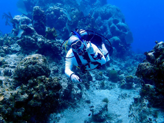 Underwater scuba diver makes the Hook 'em Horns hand sign.
