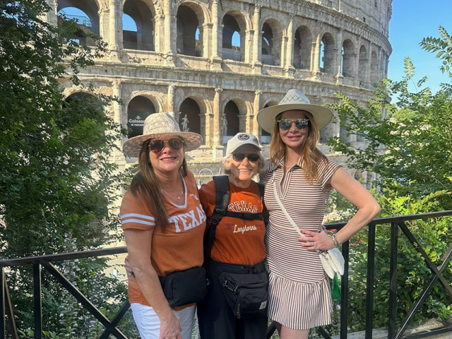 A mother and two daughters pose in burnt orange in front of the Roman Coliseum. 