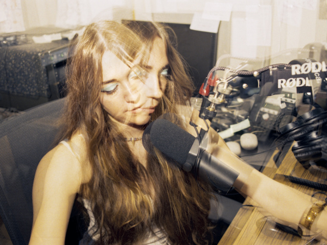 A multiple-exposure picture of a girl with blue eyeshadow and long, fringed hair, sitting in front of a radio microphone.