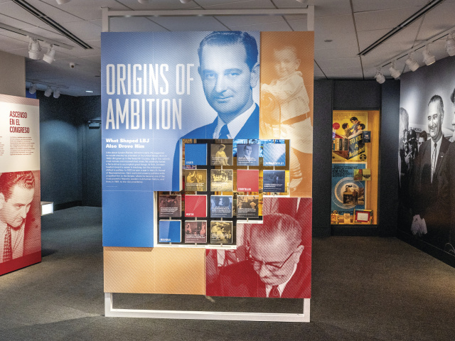 A wall at an LBJ Library exhibit reads "Origins of Ambition" with a photo of a young LBJ.