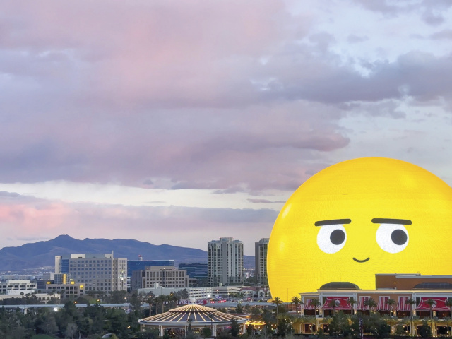 The Las Vegas Sphere, lit up as a yellow smiling emoji, against a dusky skyline.