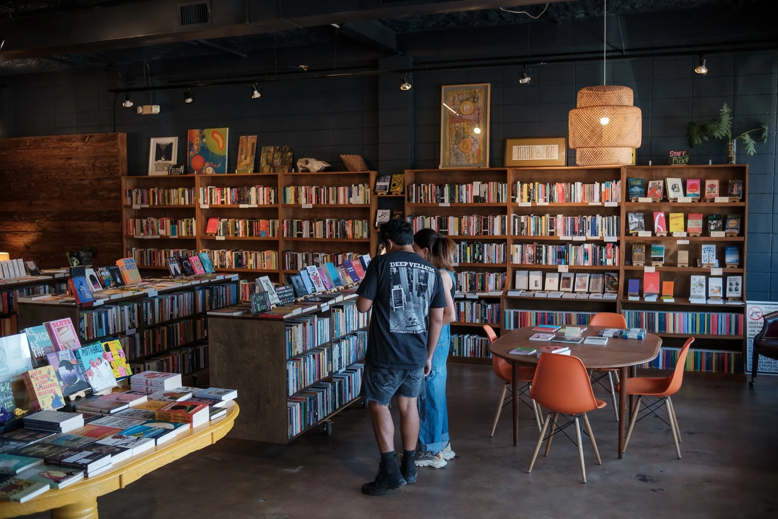 Two people look at shelves in a dim and cozy room lined with shelves.