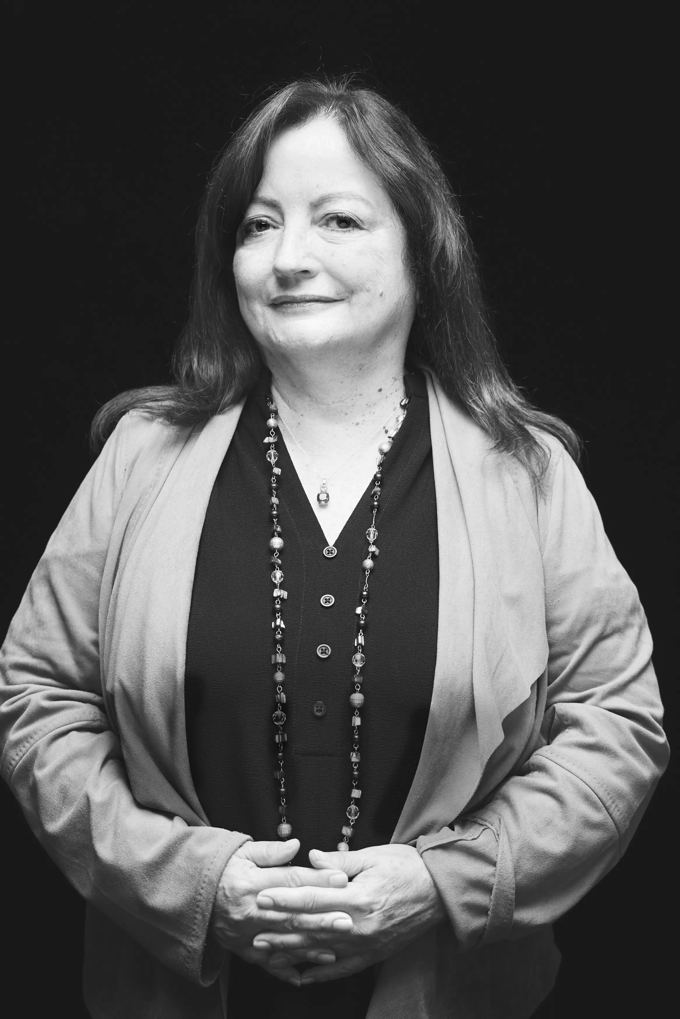 A woman stands with her hands clasped against a black background.