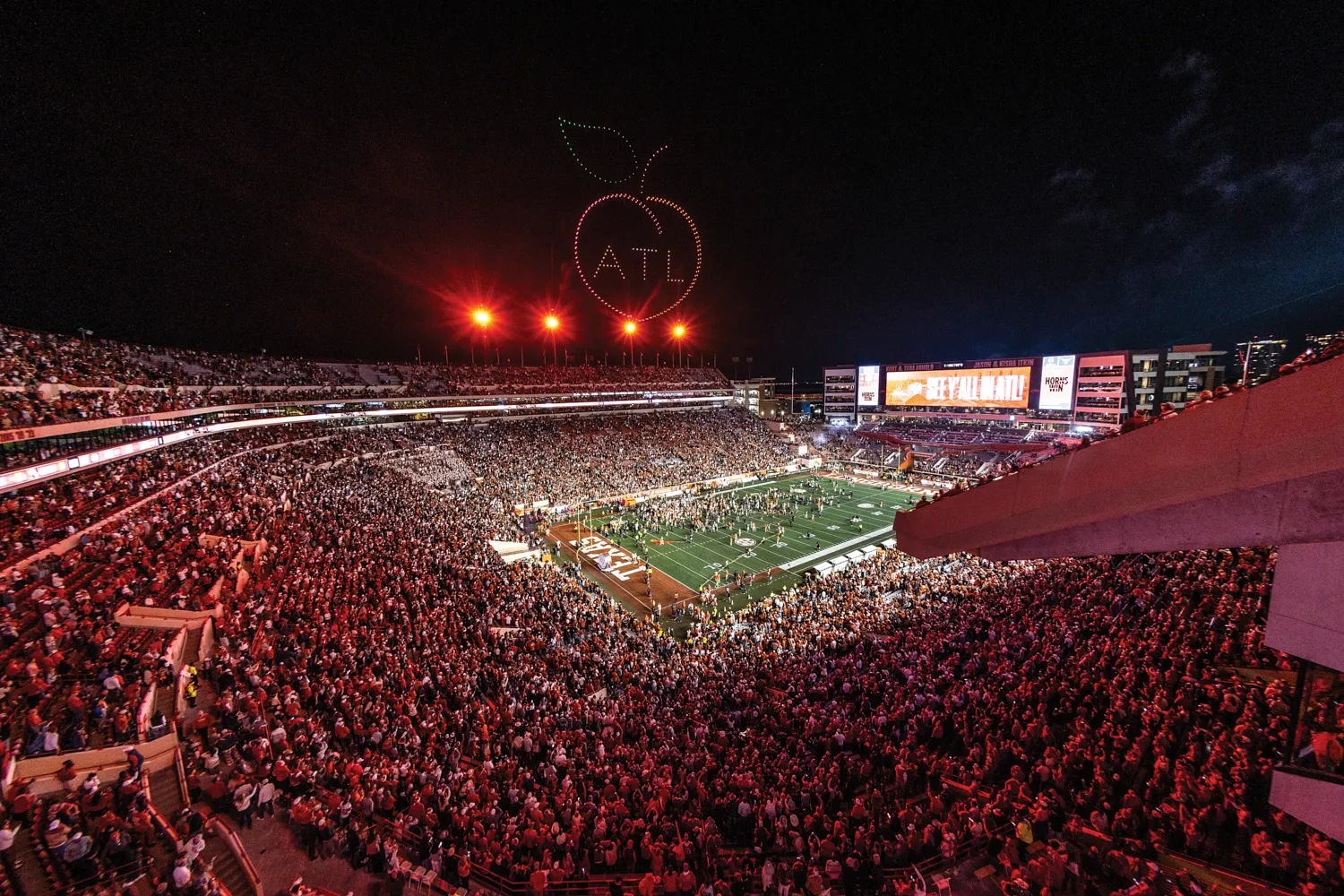 A packed football stadium with a drone show in the shape of a peach with the letters "ATL