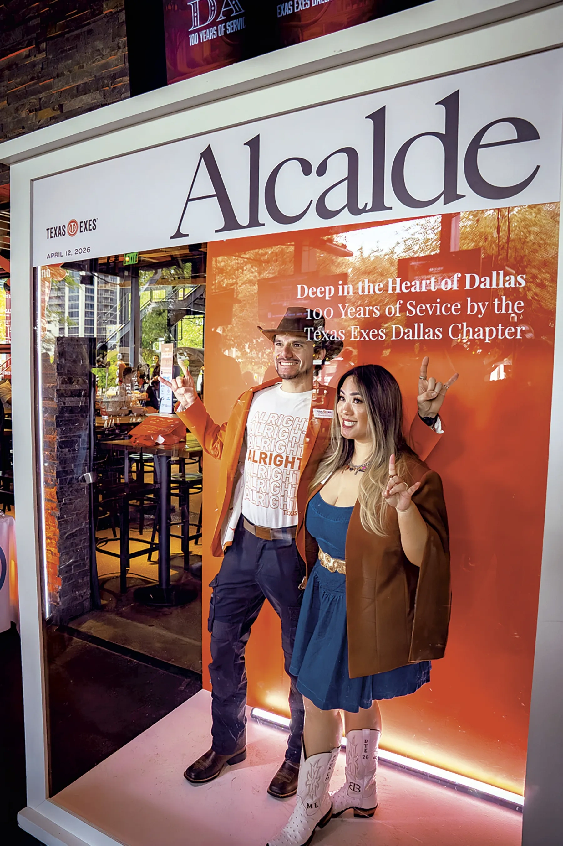 Two people pose within a life-sized magazine cover frame that reads "Alcalde."
