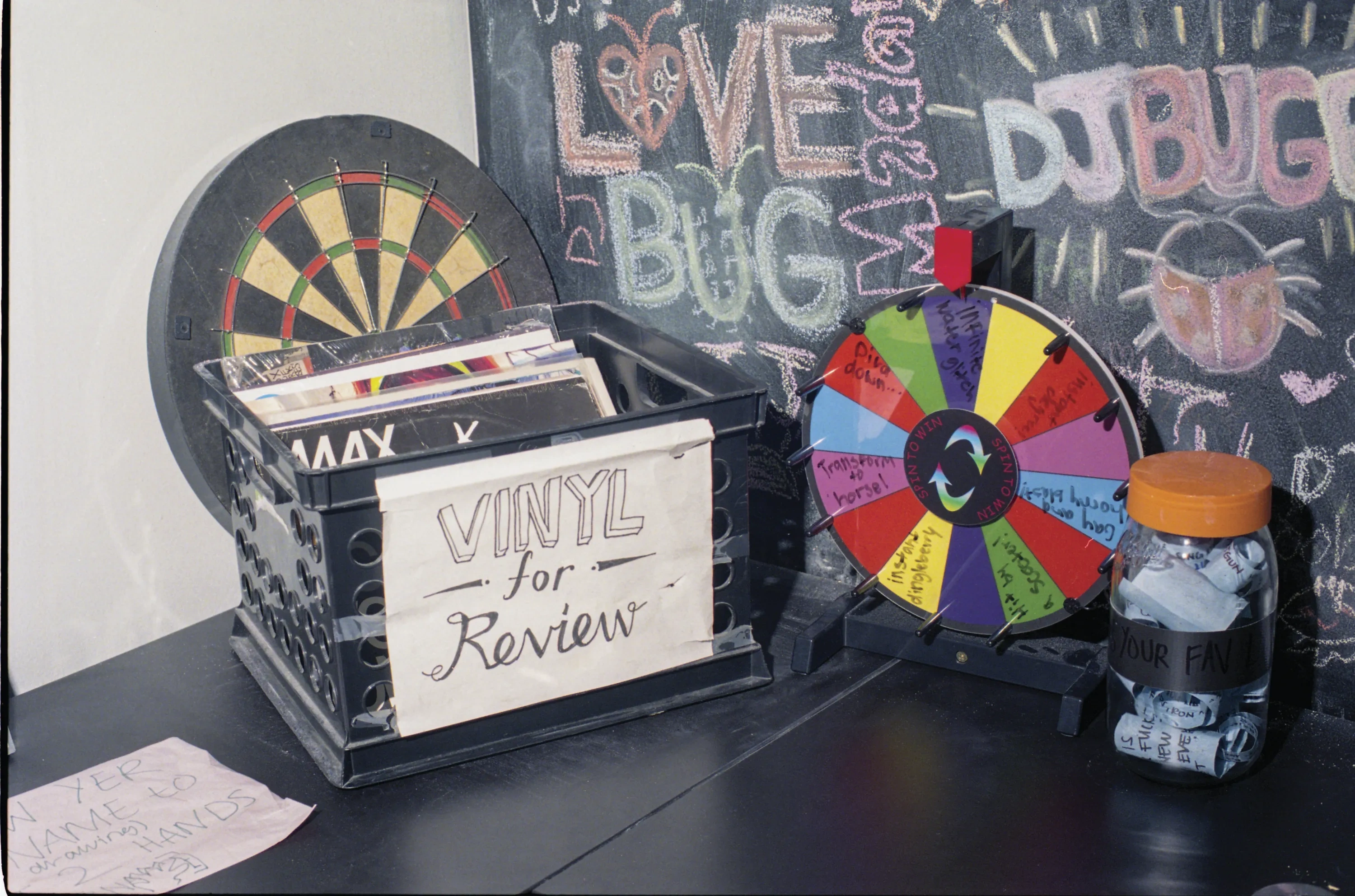 A crate of vinyl records in a black plastic crate labeled as such, against a chalk wall full of graffiti doodles.