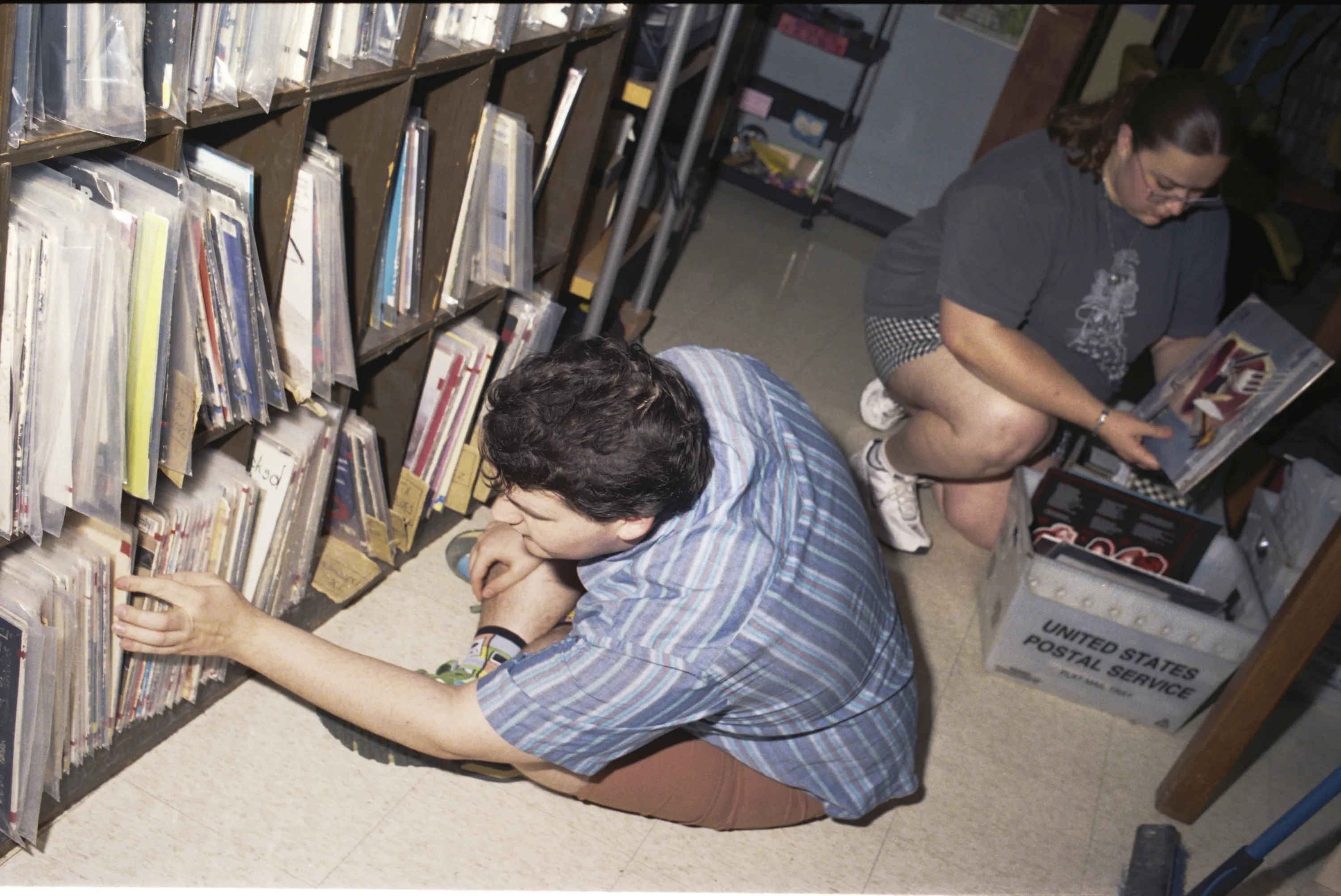 Two college students sort through vinyl records between shelves.