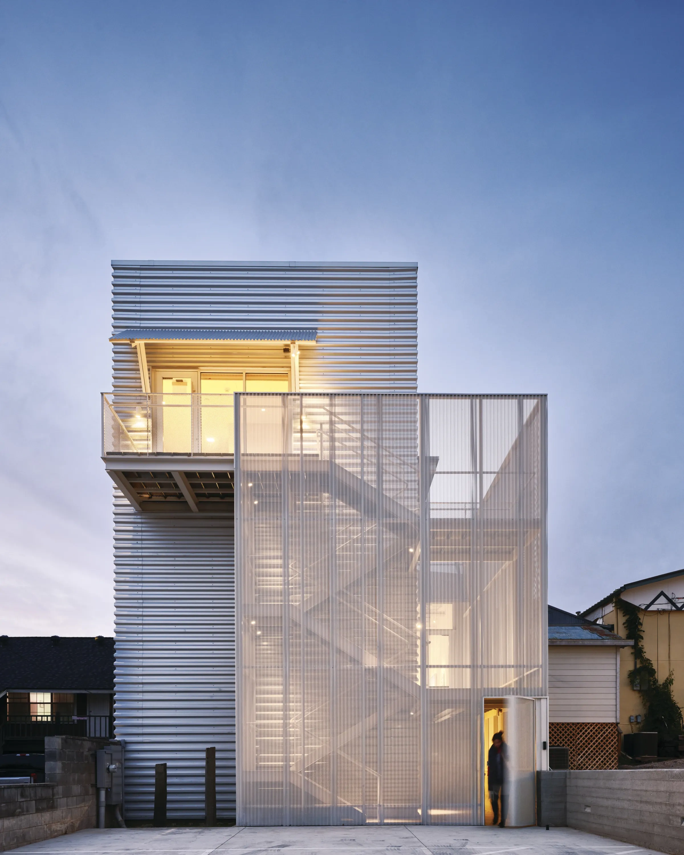 The rear facade of a modern architectural building, lit with golden light from the inside.