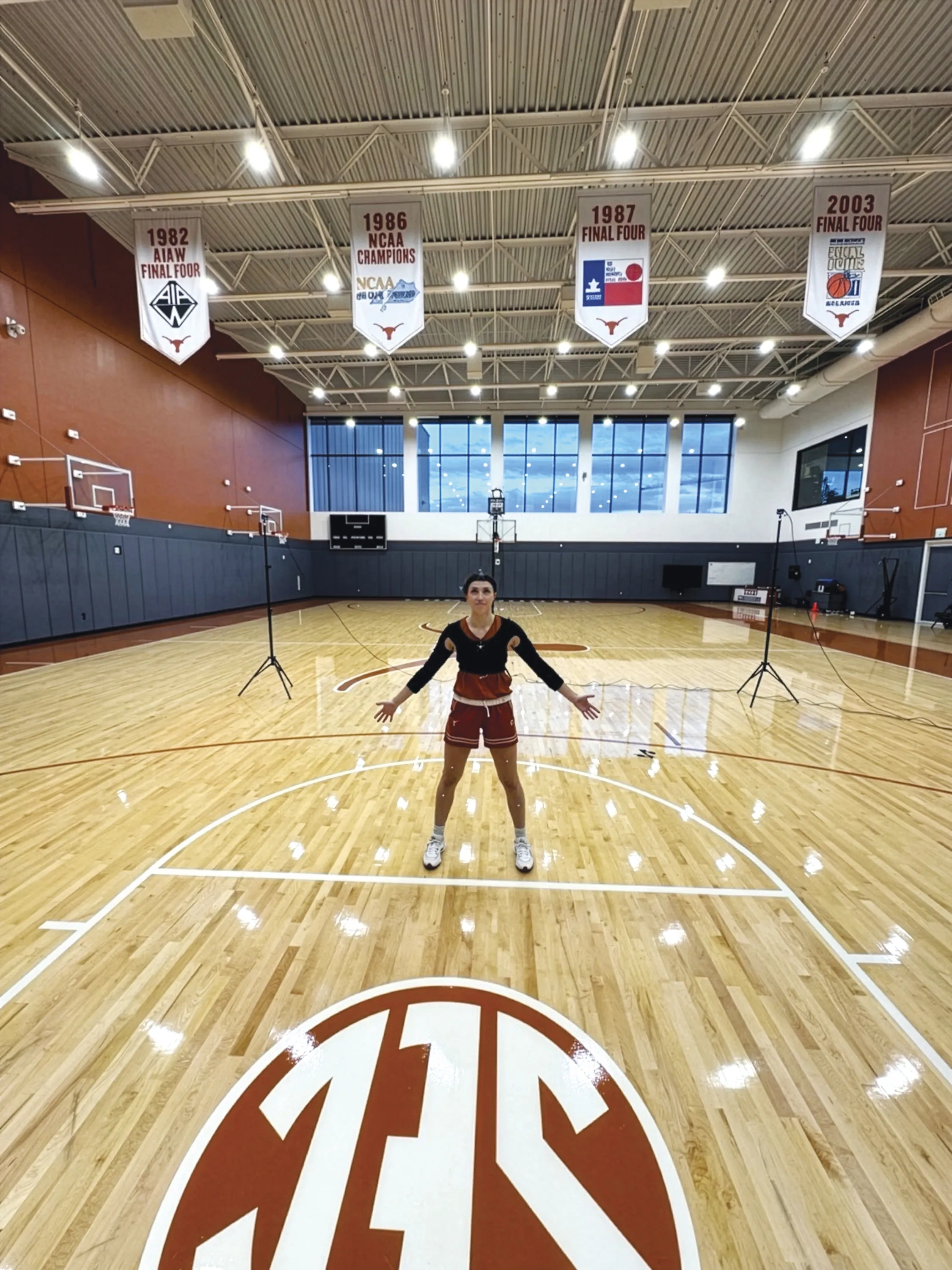 A woman stands on a basketball court wearing electronic monitoring gear.