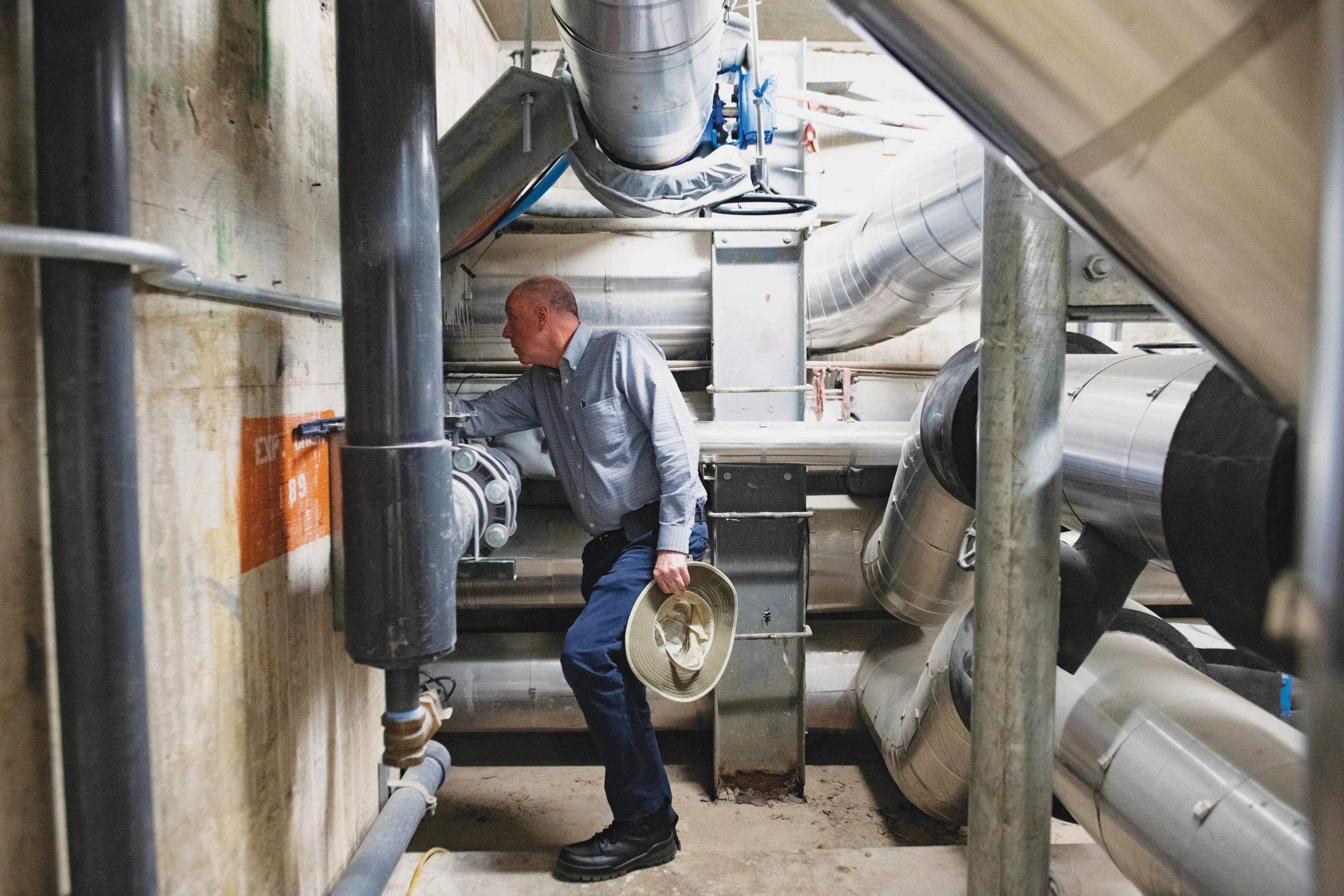 A man holds a hat while he makes an adjustment inside a power plant.
