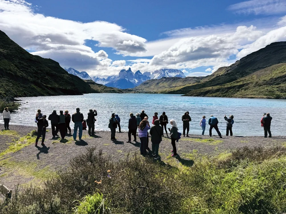 People stand looking out a lake surrounded by mountains.