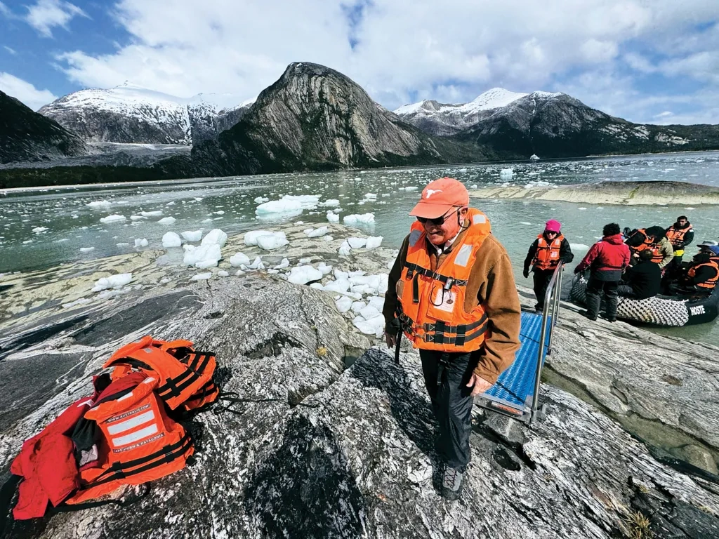 A man in a vest climbs out of a boat in icy water.