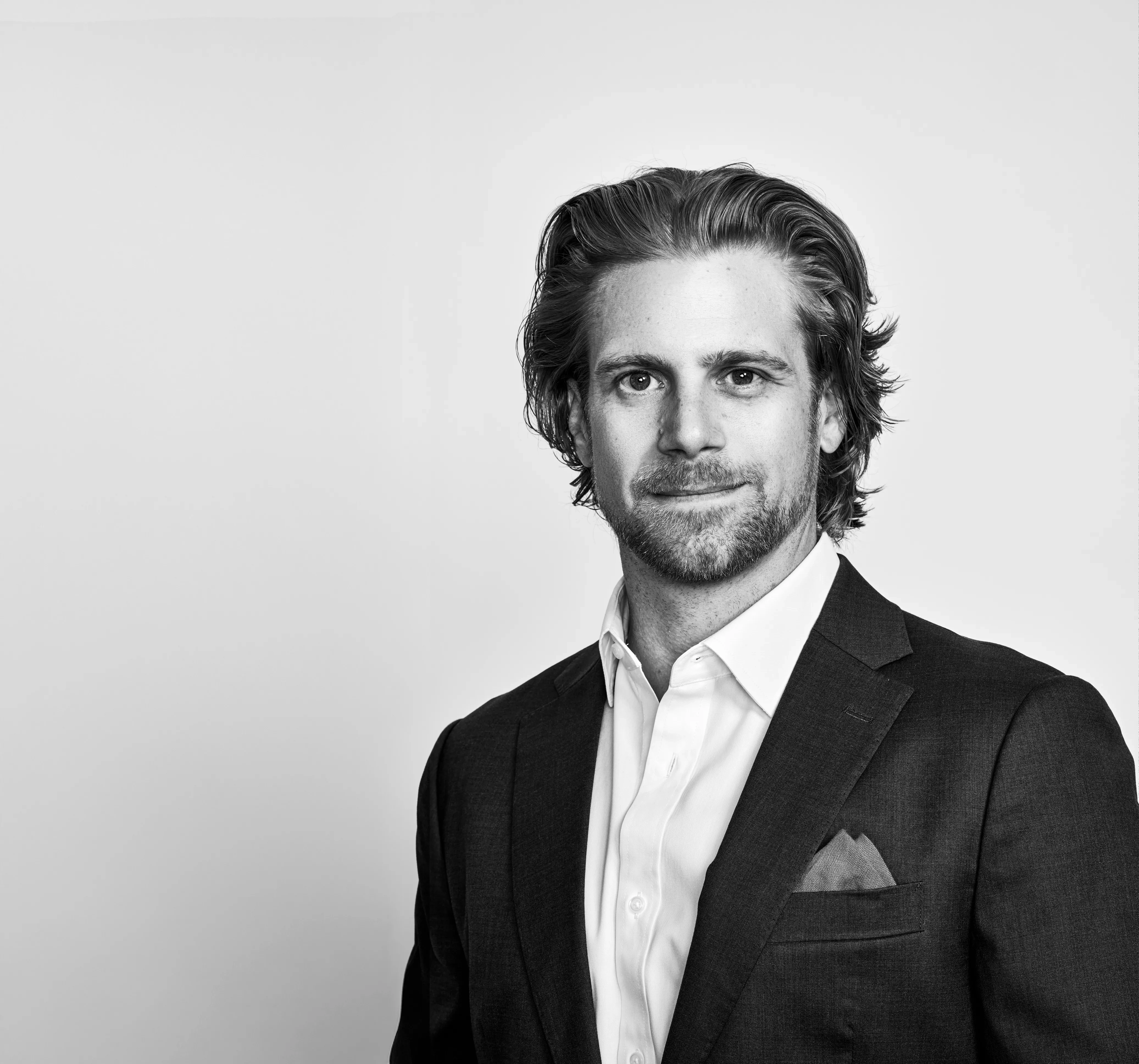 A white man with a tight beard poses on a white background in a suit with a pocket square.