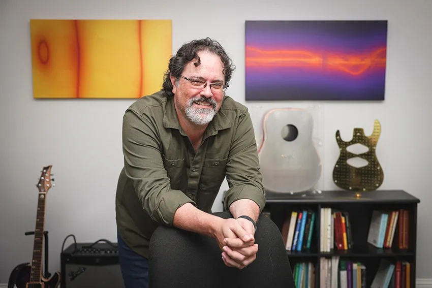 Russell Stoneback stands in front of his artwork and guitars.