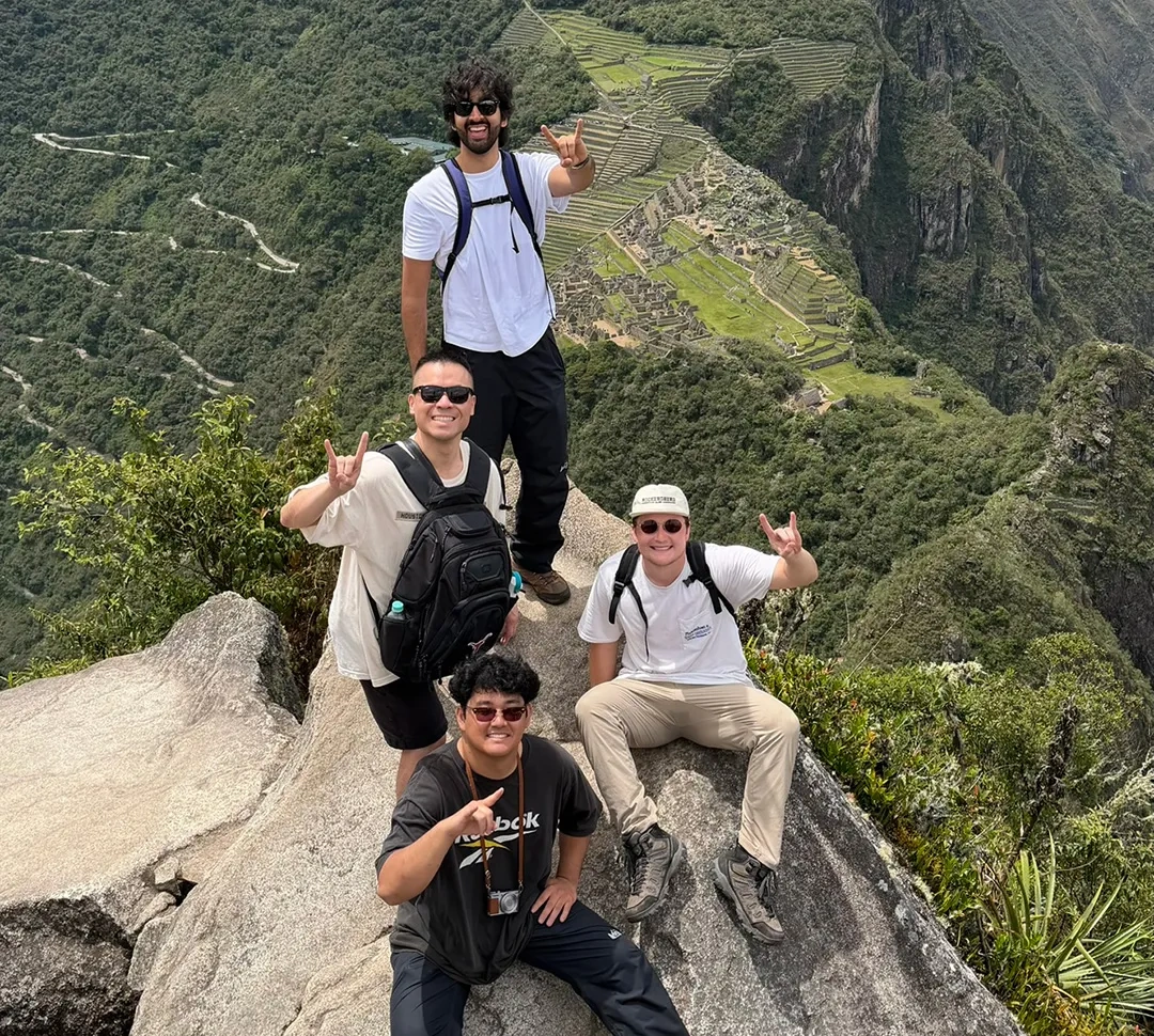 Four men high above Machu Pichu making the Hook 'em Horns hand sign.
