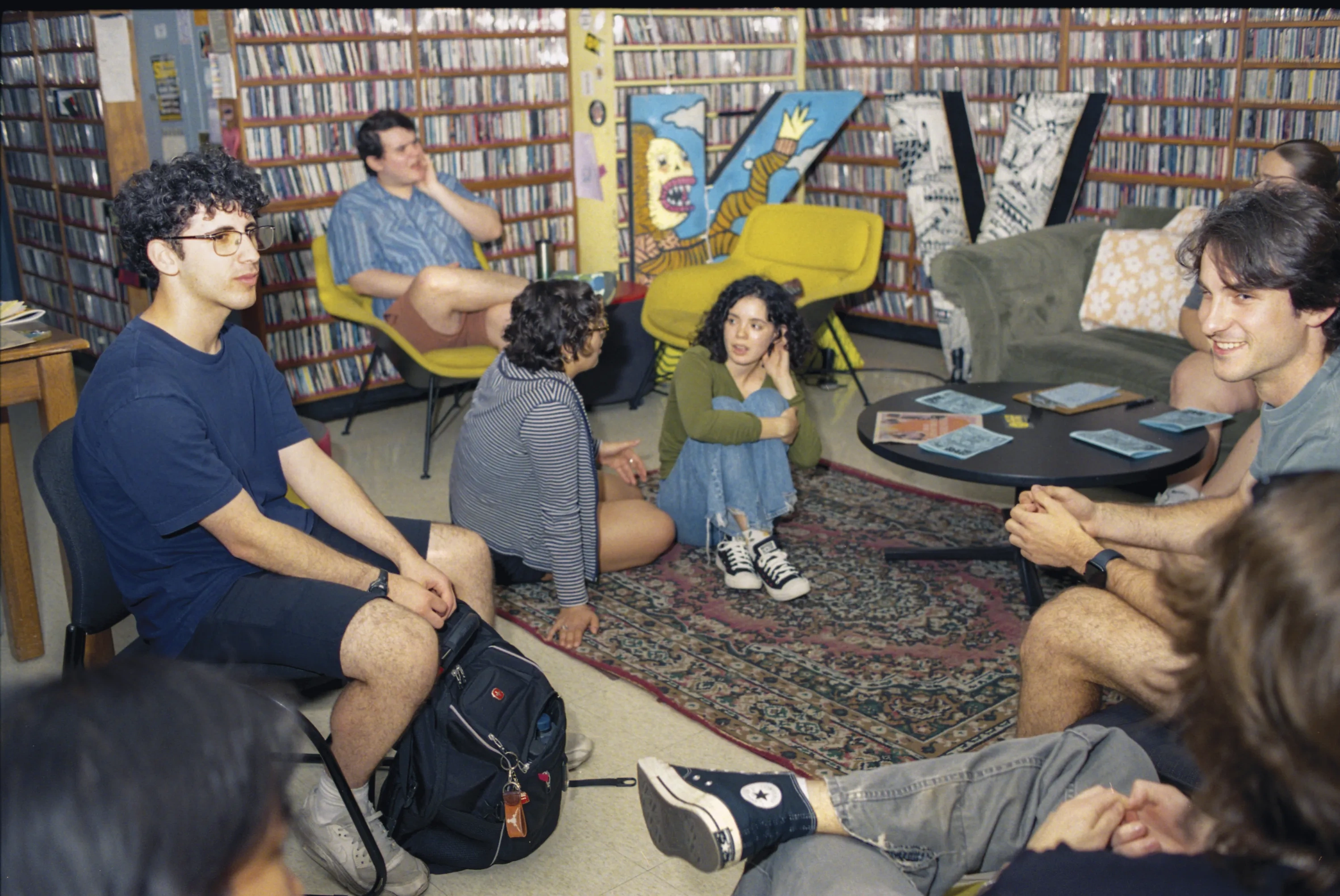 A group of students sits around a room with every wall covered in shelves of CDs and vinyl records.