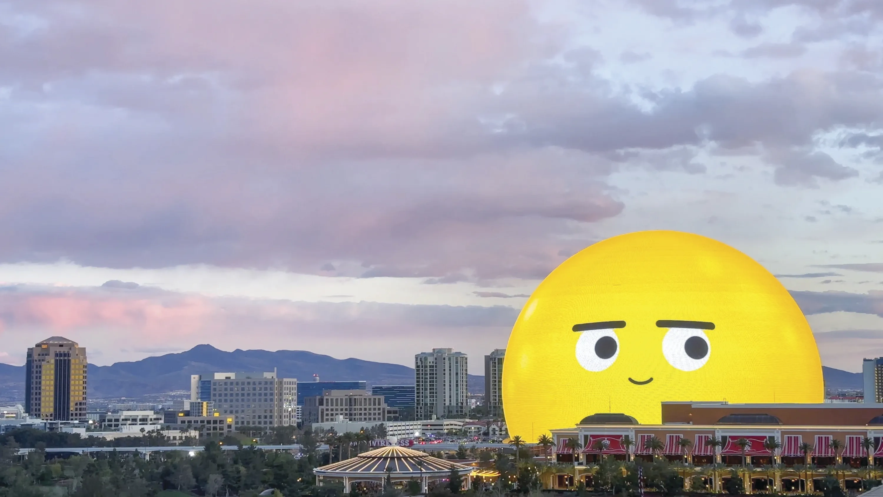 The Las Vegas Sphere, lit up as a yellow smiling emoji, against a dusky skyline.